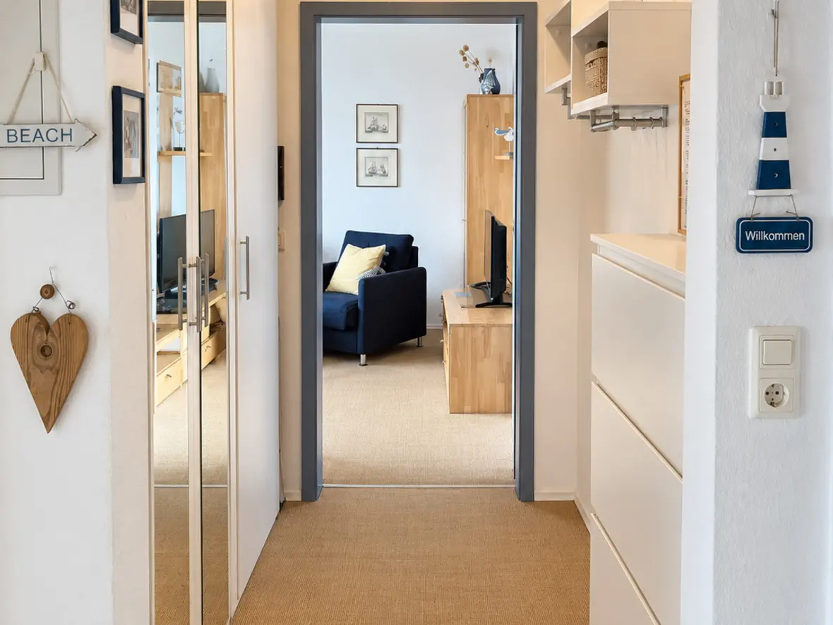 Heller Flur mit Sisalboden, verspiegeltem Kleiderschrank und maritimer Deko, am Ende der Blick ins Wohnzimmer.